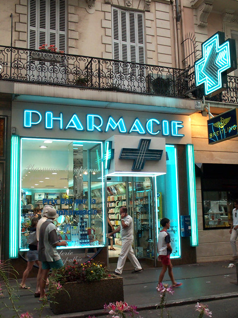 A beautifully neon lit typical French drug store (chemist) with shuttered apartments above.  Cannes, France.