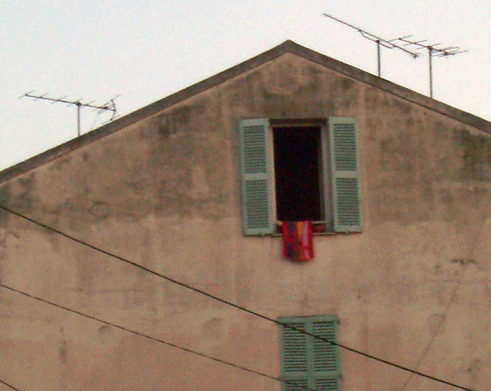 A simple French style apartment at the roof of an older building, shutters and windows open with a red towel hanging over the ledge.  Cannes, South of France.