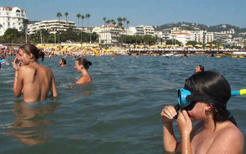 A view from inside the warm Mediterranean Sea looking back towards the beach showing several girls bathing topless.    Cannes, South of France.