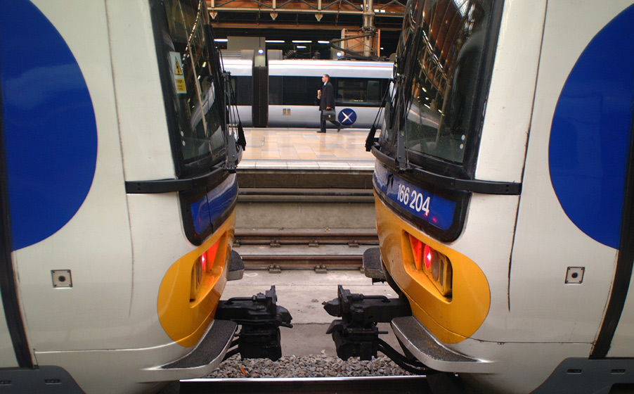 A passenger carrying a briefcase walks down the platform, as seen from between two other trains at a London railway station.  Victoria Station, London, U.K.